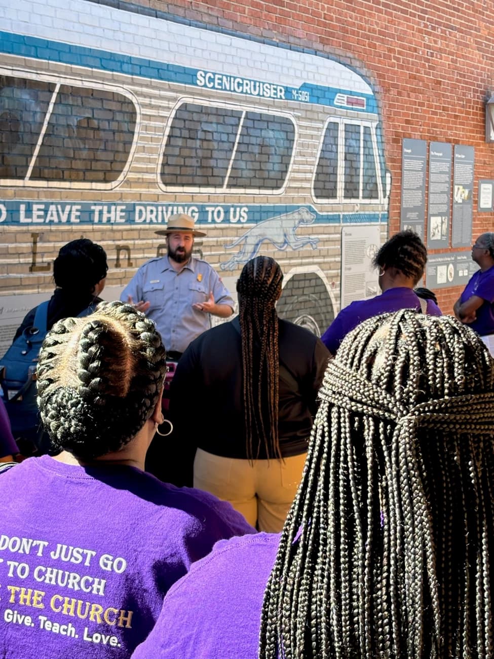 A National Park Service ranger talks to a group of visitors in front of the Freedom Riders bus mural