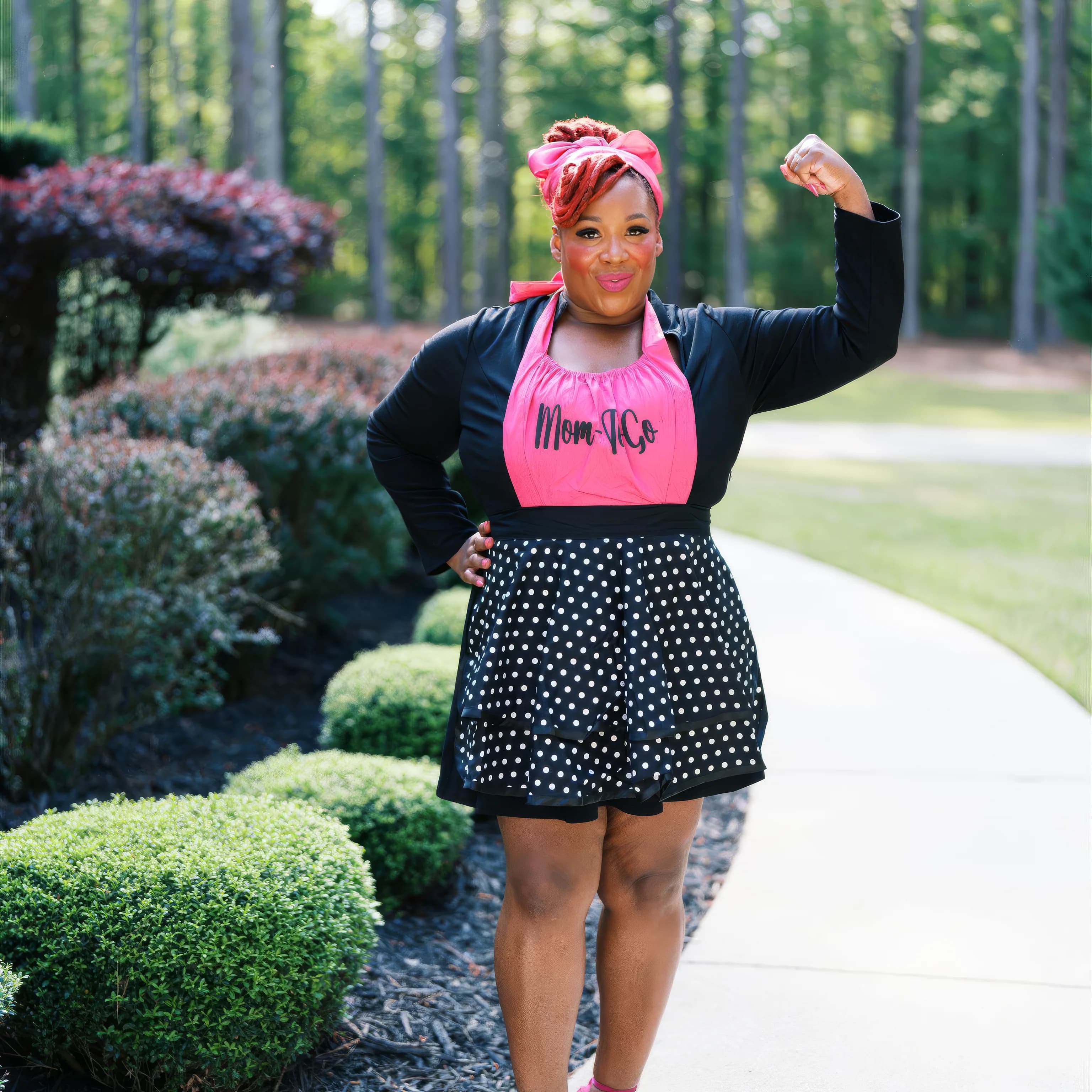 Jean Ellison in a pink Mom-To-Go apron, fist raised, outdoors in Anniston