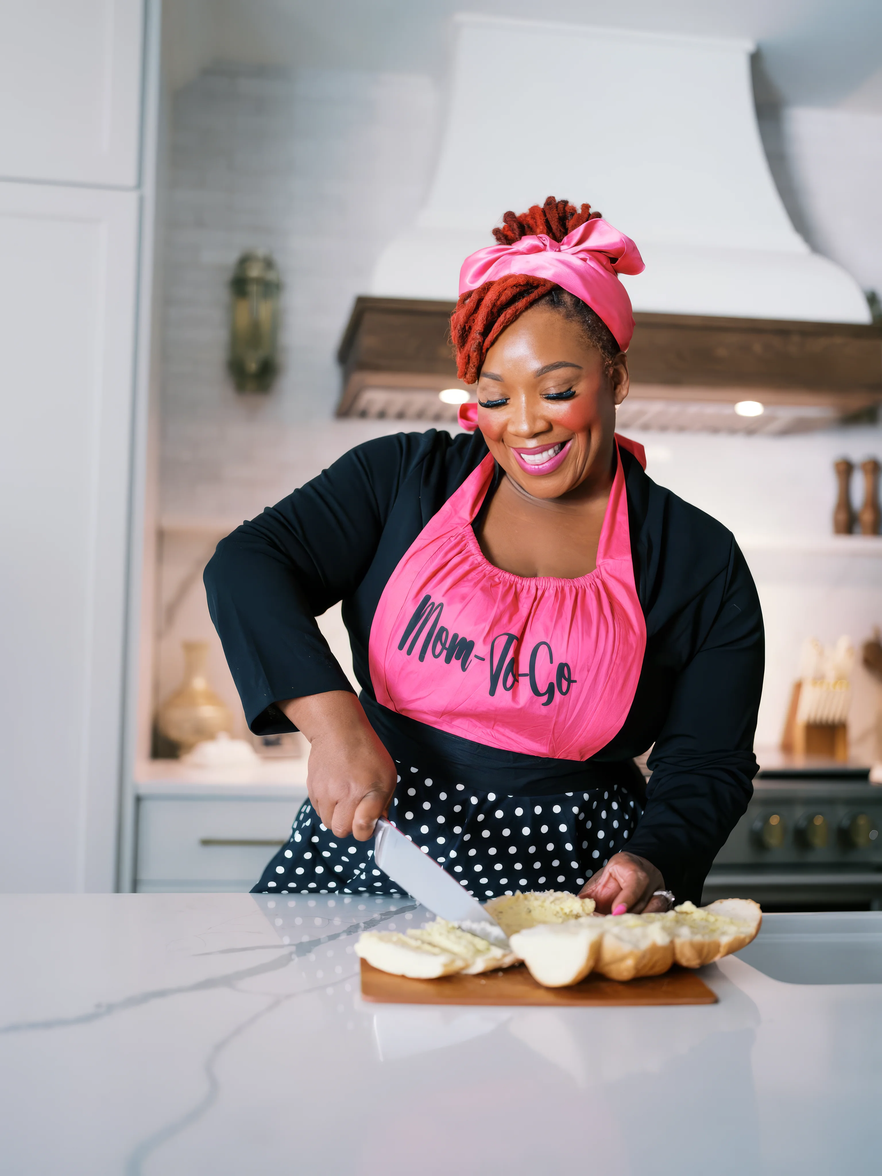 Jean Ellison in her kitchen wearing a pink Mom-To-Go apron, cutting bread