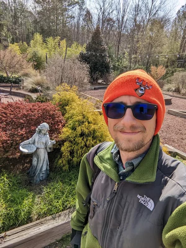 Longleaf Botanical Gardens with sculpture, raised beds, and Edison string lights visible through the trees