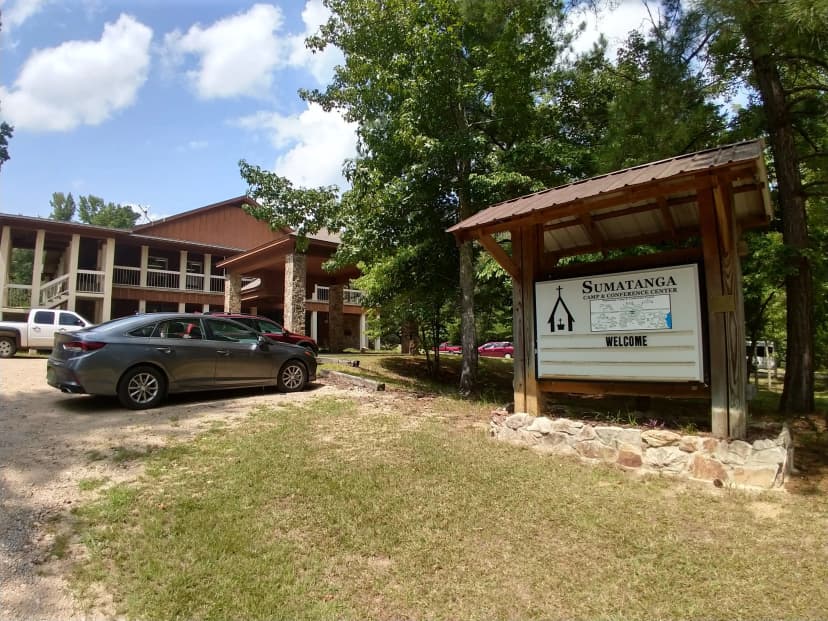 The Sumatanga Camp & Conference Center welcome sign beside the two-story lodge, cars parked in the gravel lot, summer 2018