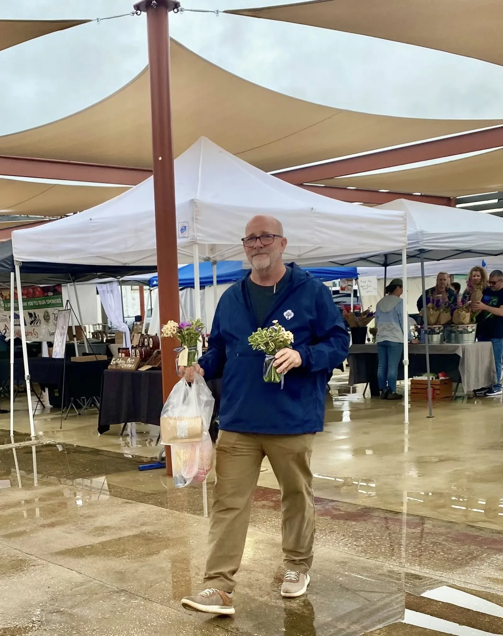 Jay Jenkins walking through the Anniston Farmers Market in the rain, carrying two bouquets