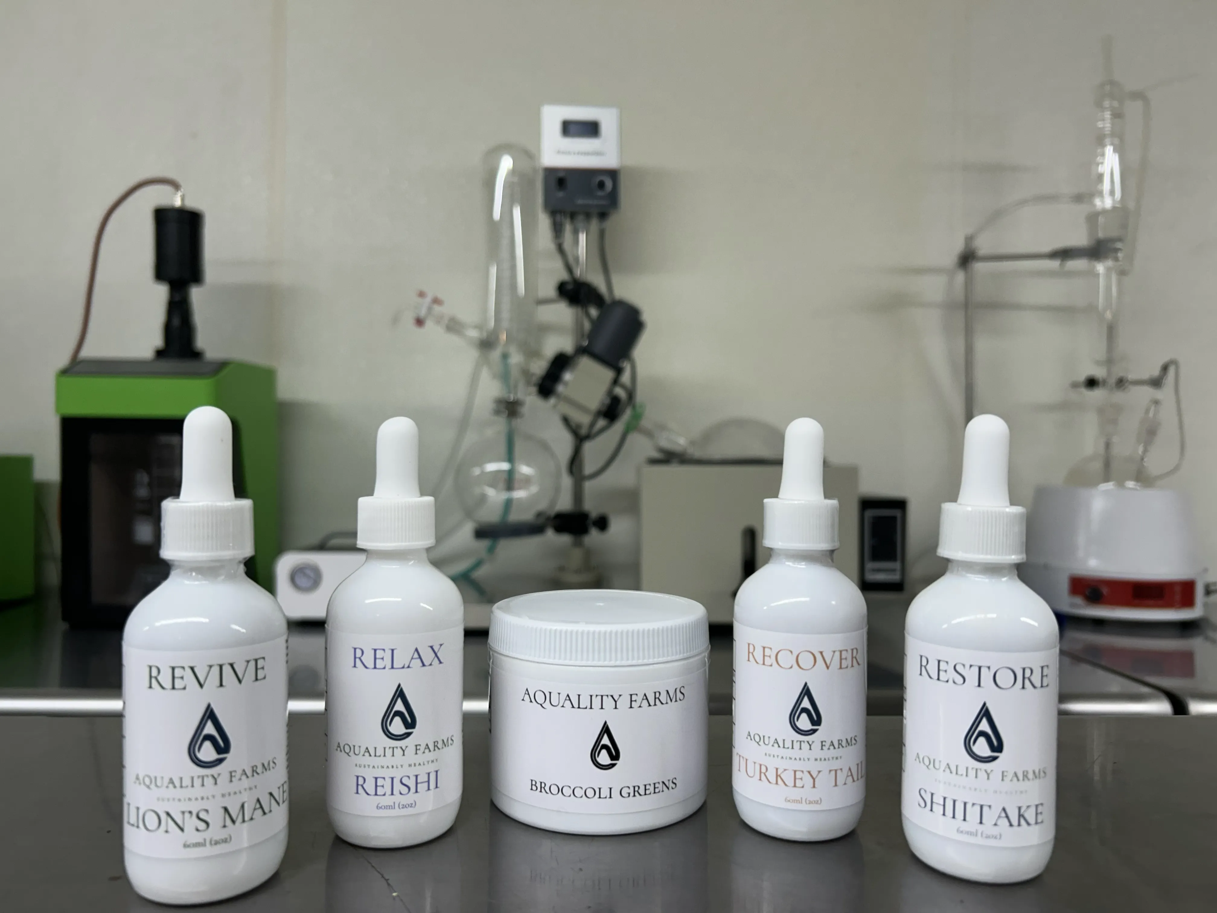 Aquality Farms tincture line — Revive, Relax, Recover, and Restore — with ultrasonic extraction equipment in the background